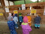 8 Kinder stehen vor einem Alpakastall. Im Stall sind 2 Alpakas