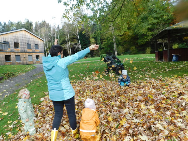 Ein Haufen voller Herbstblätter. Eine Frau spielt mit 3 Kindern in dem Haufen.
