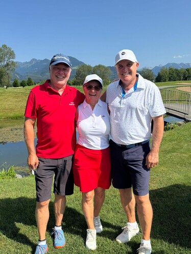 2 Männer und 1 Frau auf dem Golfplatz. Sie lächeln alle.