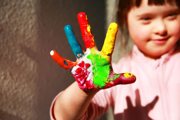 Kind streckt seine Hand voller Farbe nach vorne.