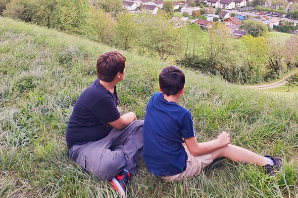 2 Jungen sitzen in der Wiese mit Blick Richtung Dorf