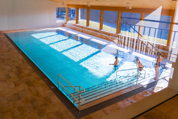 Hallenbad von oben, 2 Personen sind im Wasser, 1 Person steht am Beckenrand